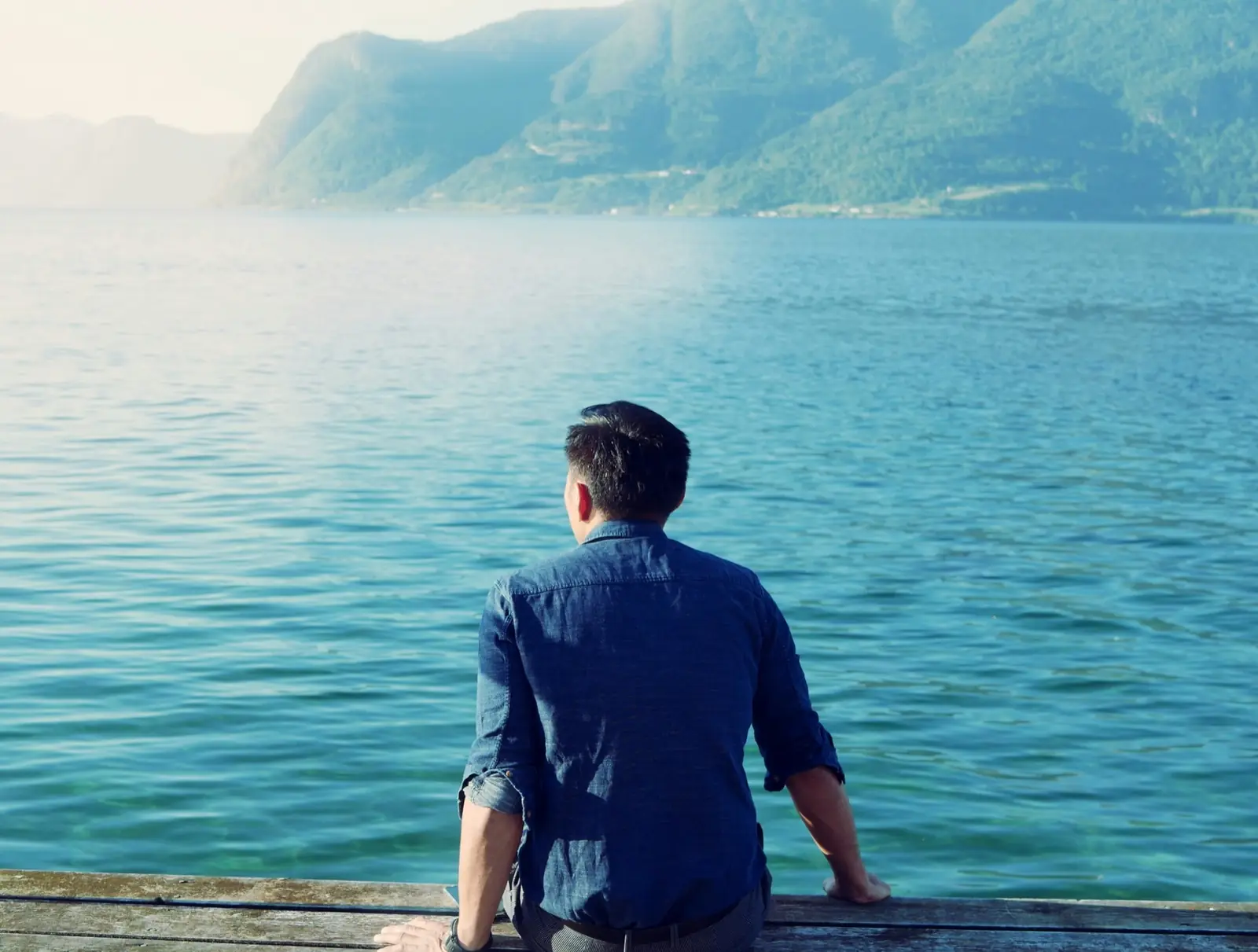 Un homme assis face à un lac calme, dos tourné