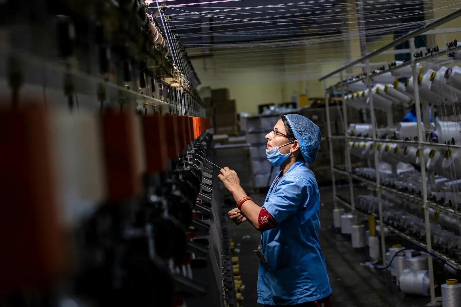 Une ouvrière contrôle les fils sur une grande machine textile