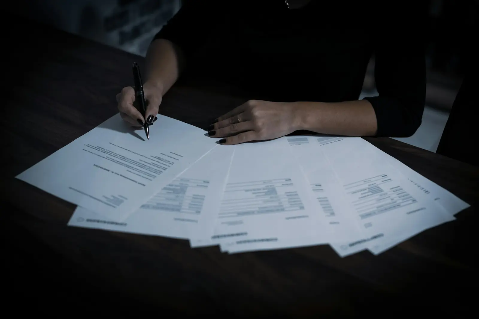 Une femme signe un contrat au stylo, entourée de papiers