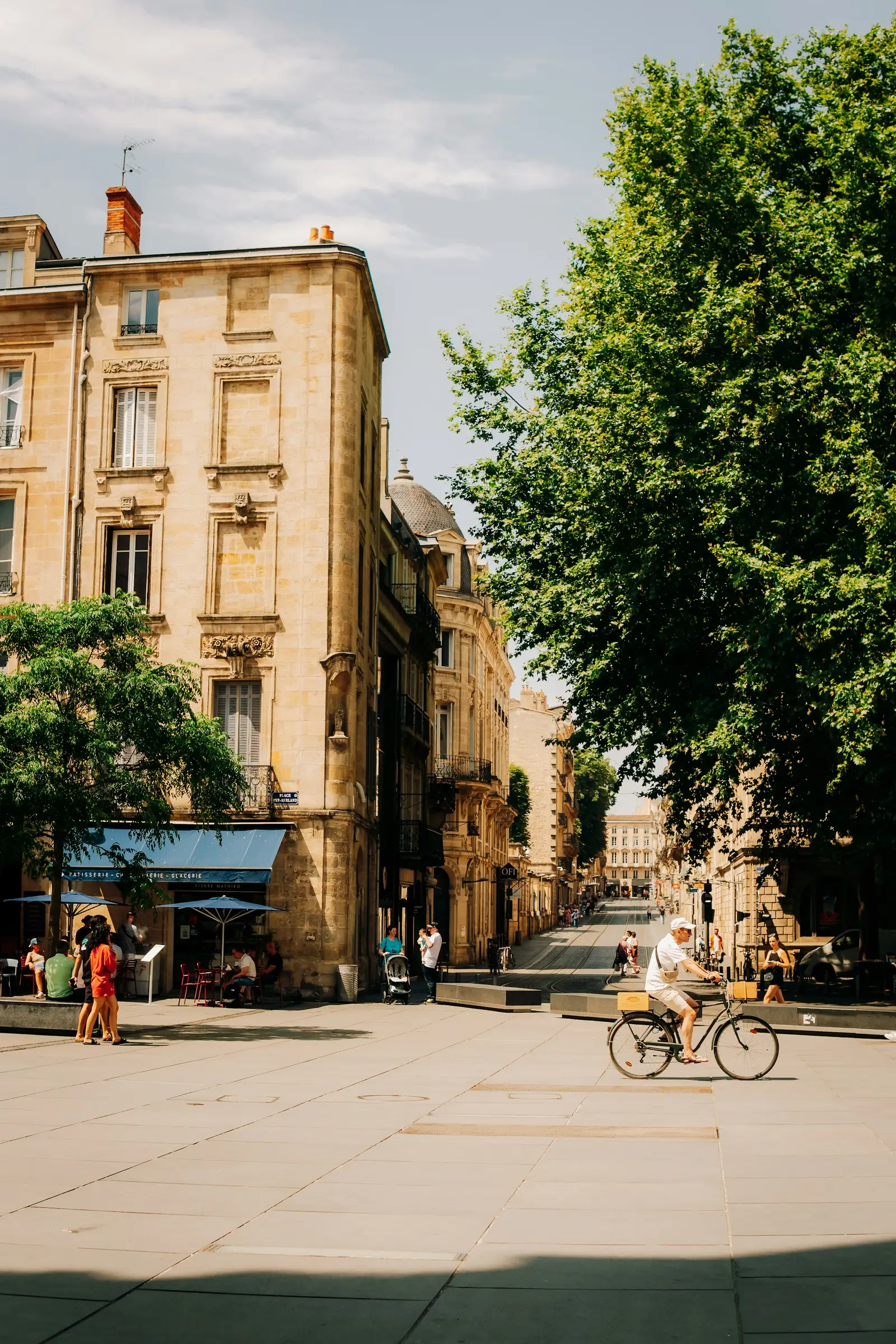 Un homme traverse à vélo une place ensoleillée de Bordeaux